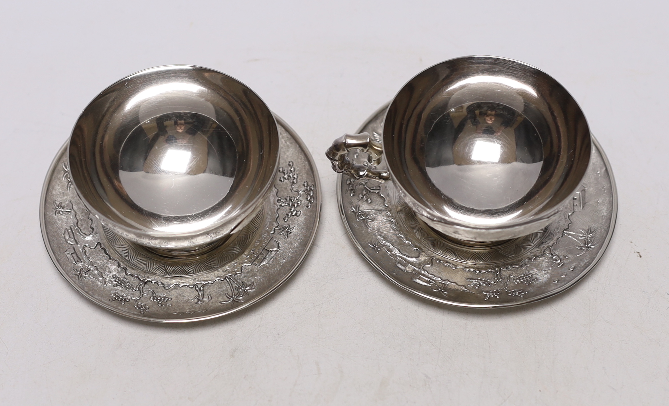 Two early 20th century Vietnamese 800 standard white metal tea cups and saucers (one lacking handle), saucer diameter 10.1cm, 6.6oz.